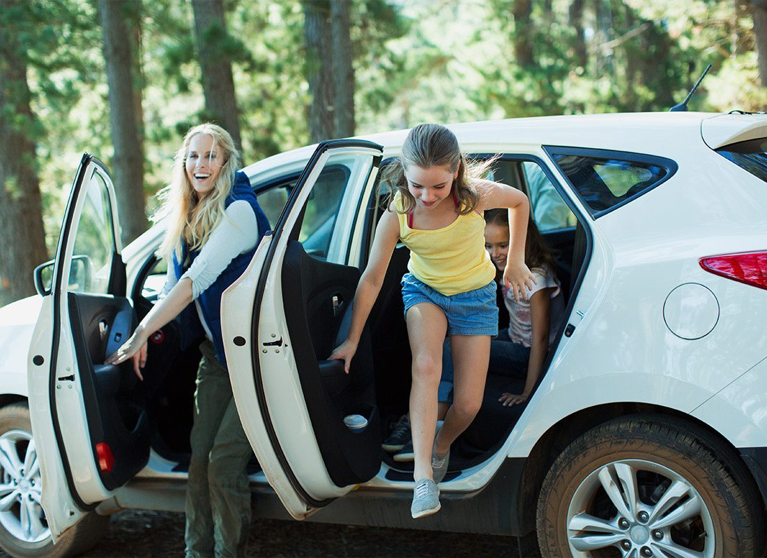 Insurance Solutions - Mom and Daughters Exiting Their Car For a Camping Trip in the Forest on a Nice Day