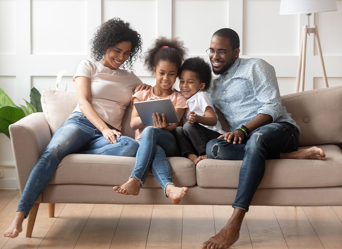Personal Insurance - A Smiling Family Sitting Together on the Couch in Their Living Room While Holding a Tablet